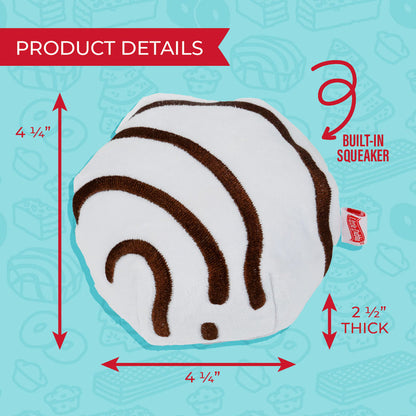 A Little Debbie Zebra Cake dog toy with labeled product dimensions and features. The round toy has a white base with brown zebra-like stripes, resembling the iconic Zebra Cake snack. Measurements indicate it is 4 1/4 inches tall, 4 1/4 inches wide, and 2 1/2 inches thick. An arrow points to a “built-in squeaker” feature on the right. A small red Little Debbie logo tag is attached to the side. The background is light blue with faint outlines of various Little Debbie snacks.